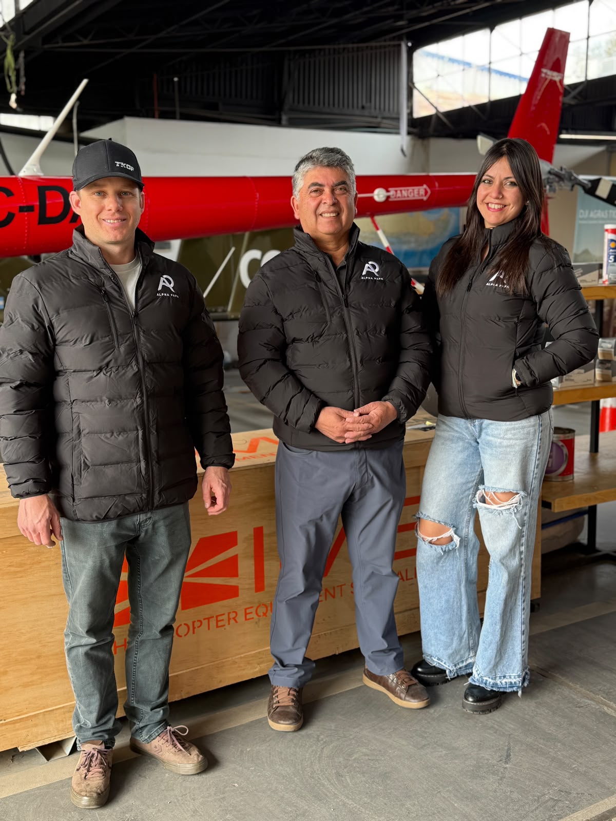 Equipo de Alpha Papa en hangar frente a helicóptero vistiendo parkas corporativas térmicas negras con logotipo bordado